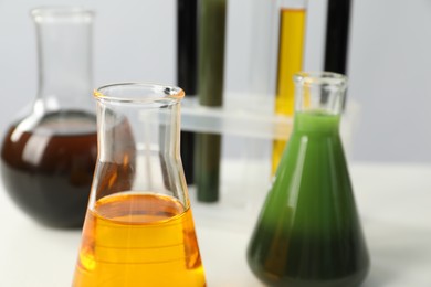 Laboratory glassware with different types of oil on white table, closeup