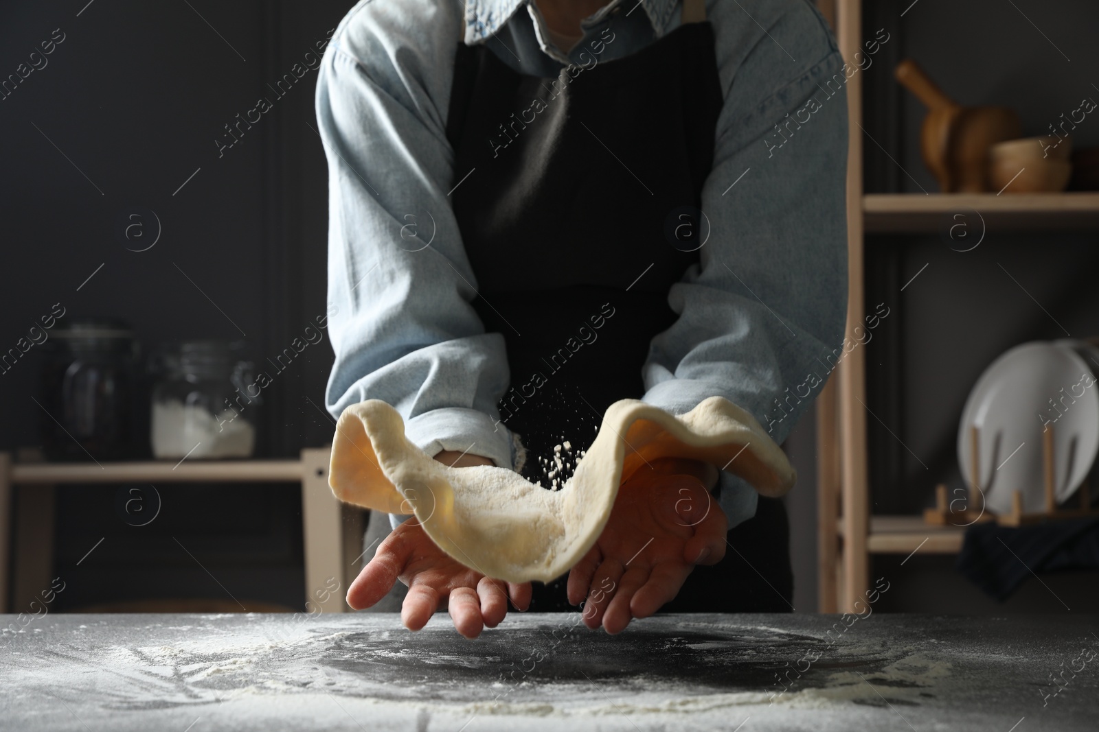 Photo of Woman tossing pizza dough at table in kitchen, closeup