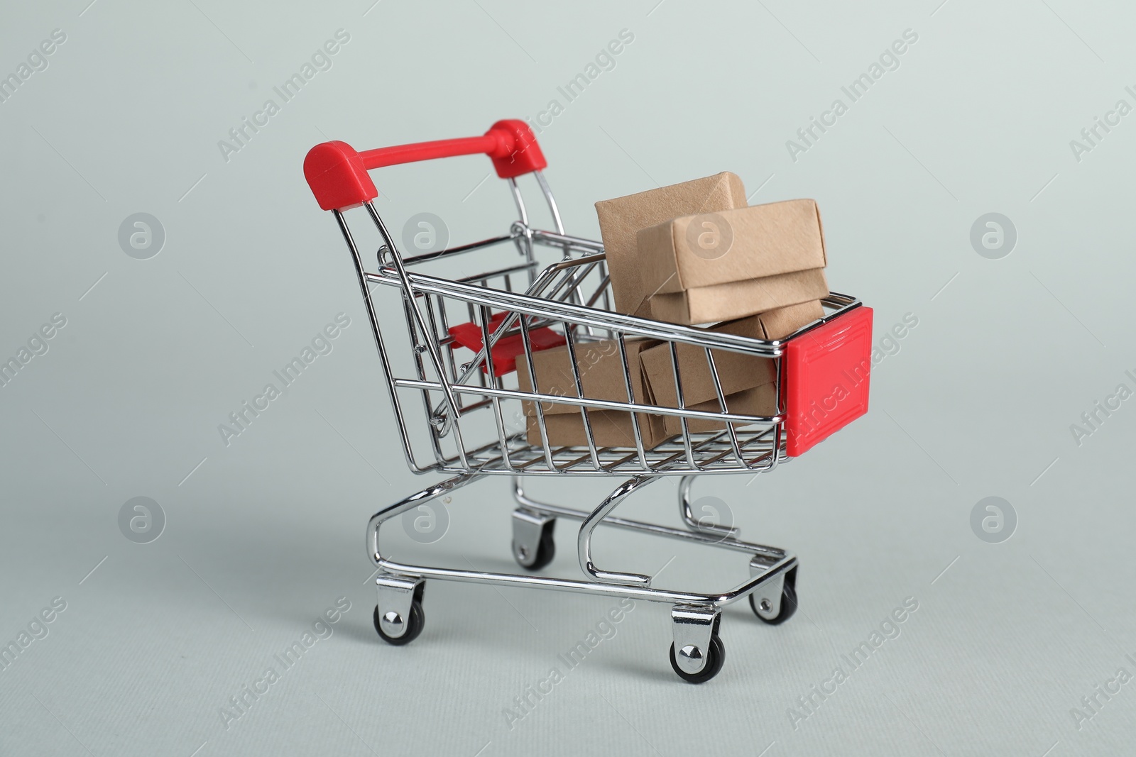 Photo of Small metal shopping cart with cardboard boxes on light background