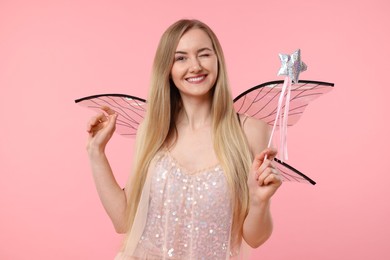 Beautiful girl in fairy costume with wings and magic wand winking on pink background