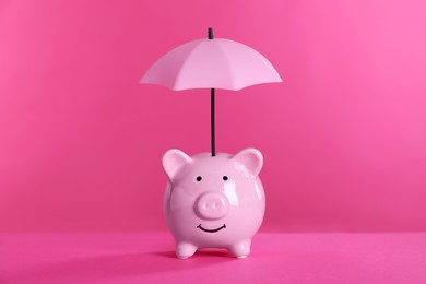 Photo of Small umbrella and piggy bank on pink background