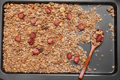 Photo of Making granola. Mixture of oat flakes, other ingredients and spoon on baking tray, flat lay
