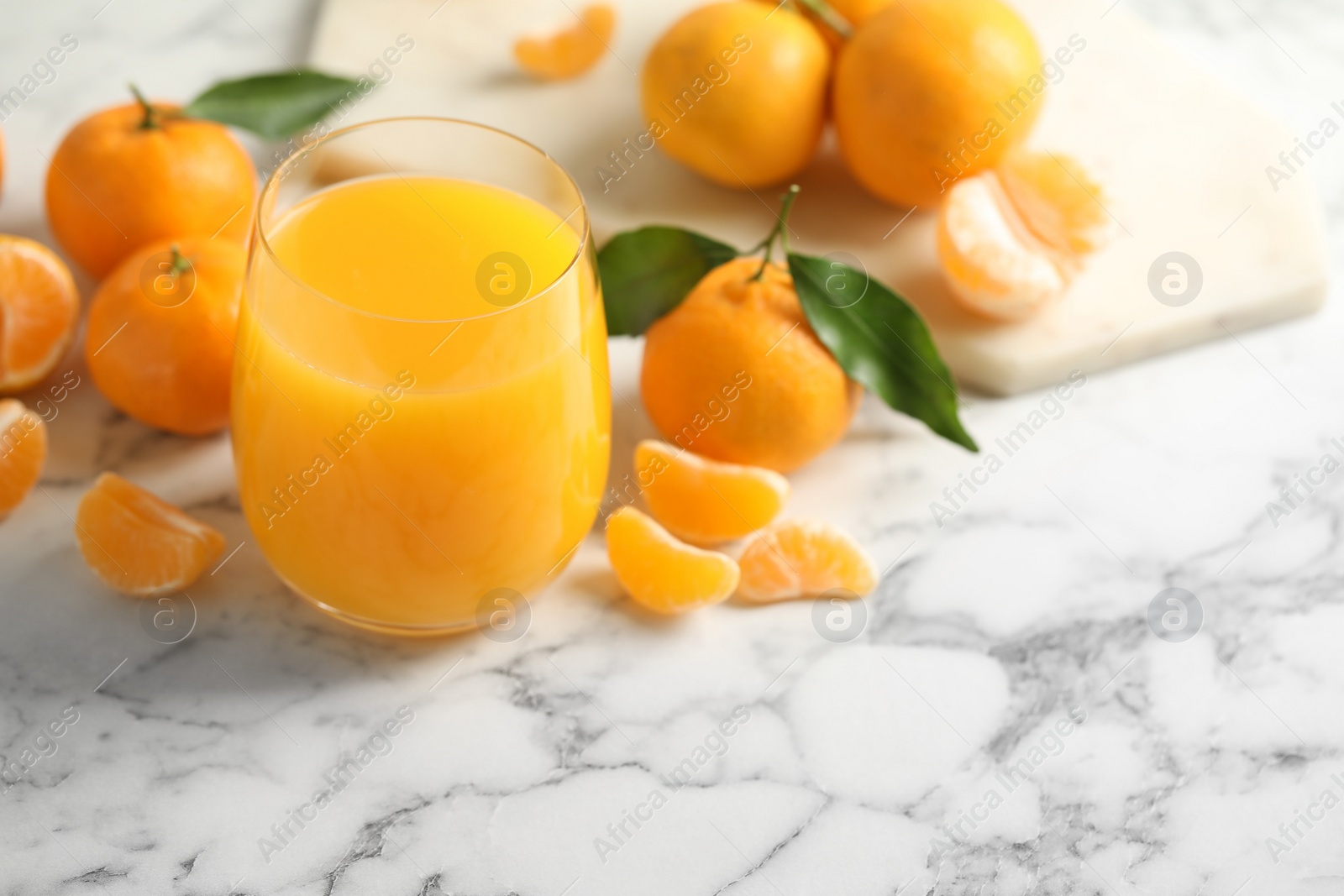 Photo of Glass of fresh tangerine juice and fruits on marble table. Space for text