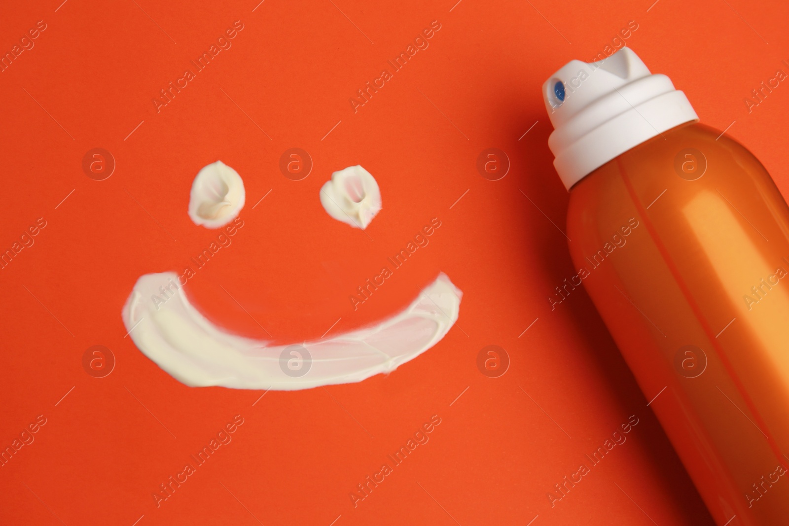 Photo of Drawing of smiling face and bottle with sunscreen on coral background, top view. Sun protection care