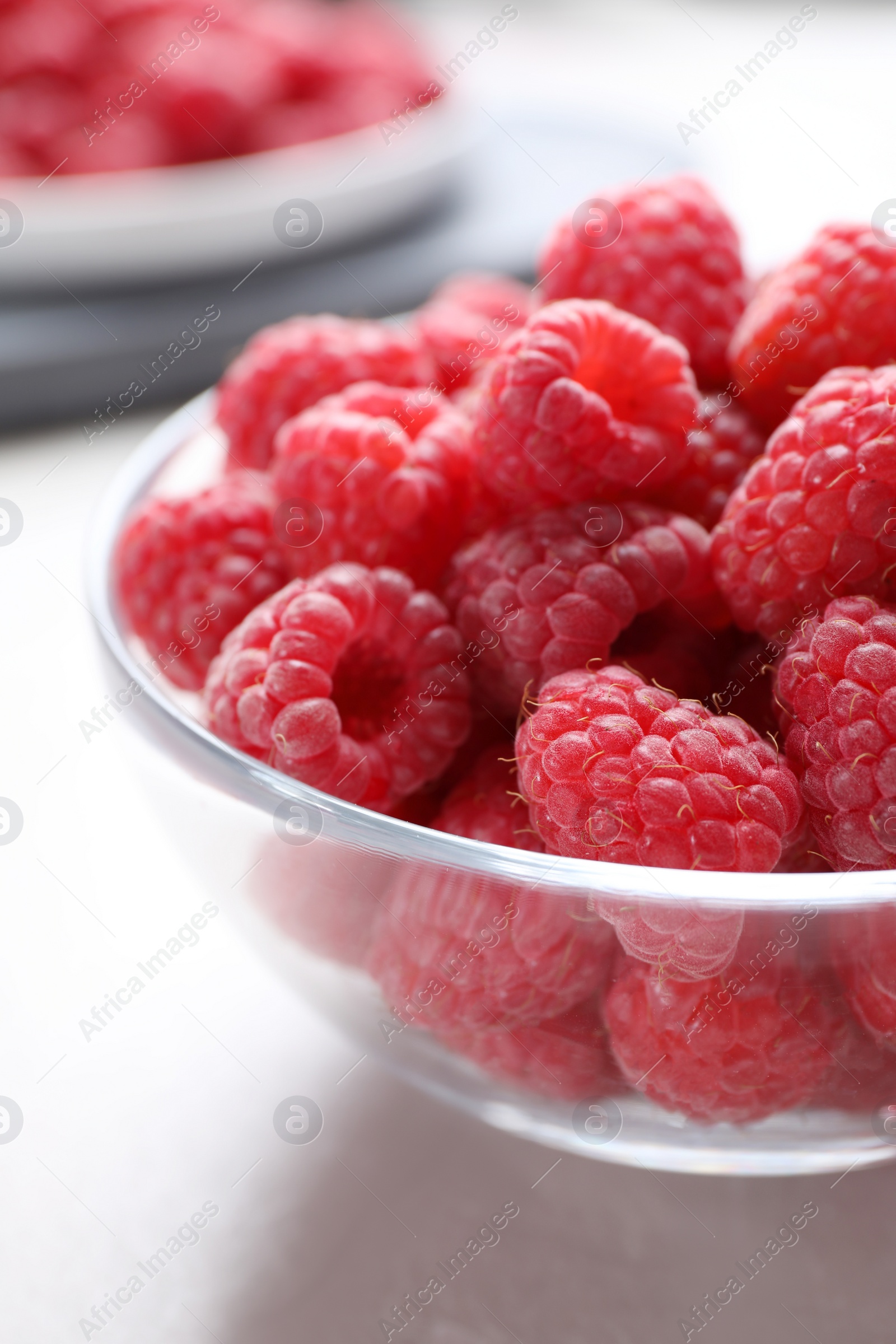 Photo of Delicious fresh ripe raspberries in glass bowl on white table, closeup