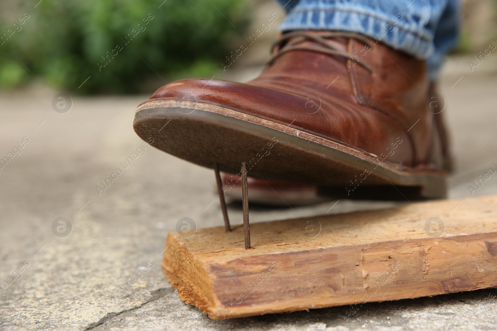 Photo of Careless man stepping on nails in wooden plank outdoors, closeup