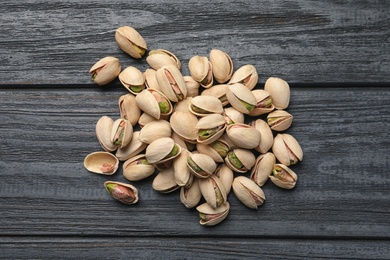 Photo of Heap of organic pistachio nuts on wooden table, top view