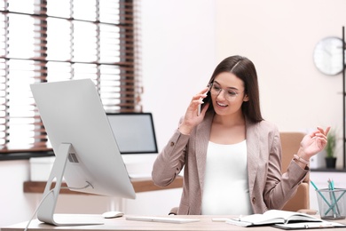 Photo of Young pregnant woman talking on phone while working in office