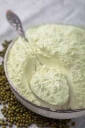 Photo of Bowl of flour, spoon and mung beans on light grey cloth, closeup