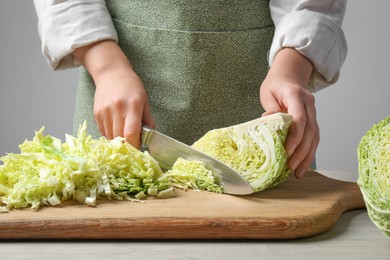 Photo of Woman cutting fresh savoy cabbage on board at wooden table, closeup