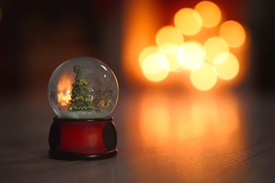 Snow globe on wooden table against blurred background, space for text. Bokeh effect