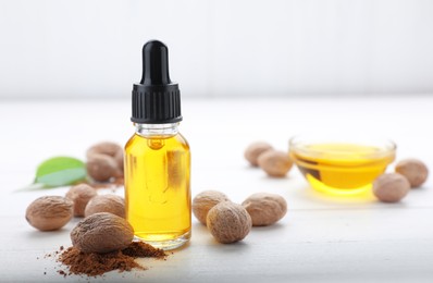 Photo of Bottle of nutmeg oil, nuts and powder on white wooden table, space for text