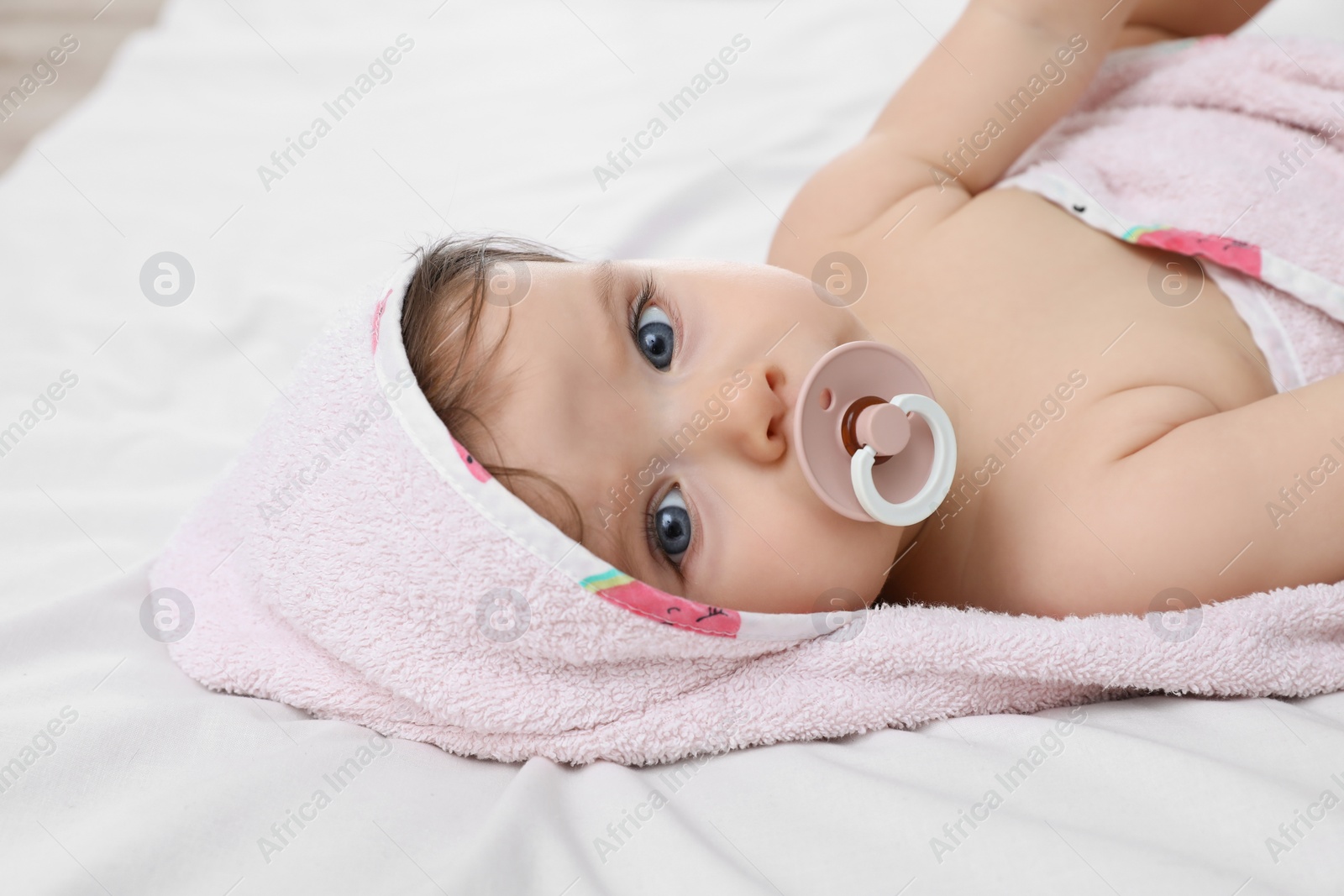 Photo of Cute little baby with pacifier in hooded towel after bathing on bed