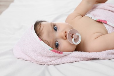 Cute little baby with pacifier in hooded towel after bathing on bed