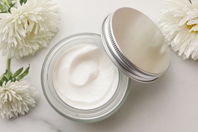 Photo of Glass jar of face cream and flowers on white marble table, flat lay