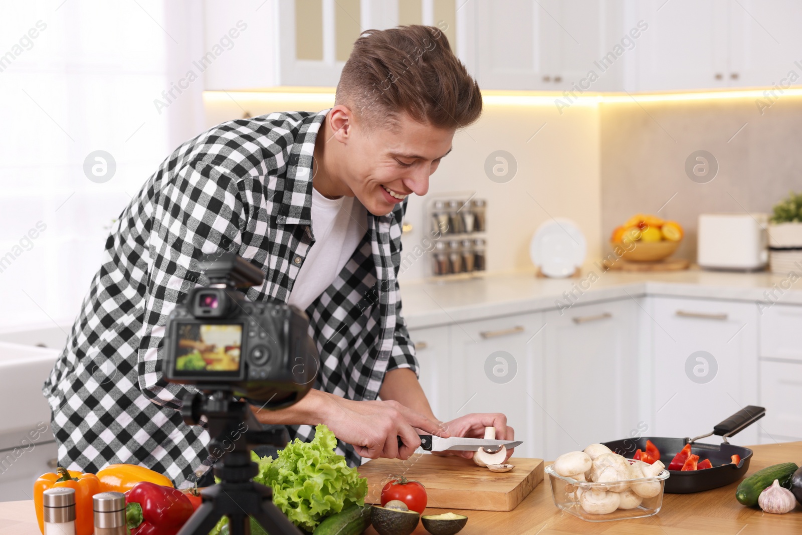 Photo of Smiling food blogger cooking while recording video in kitchen