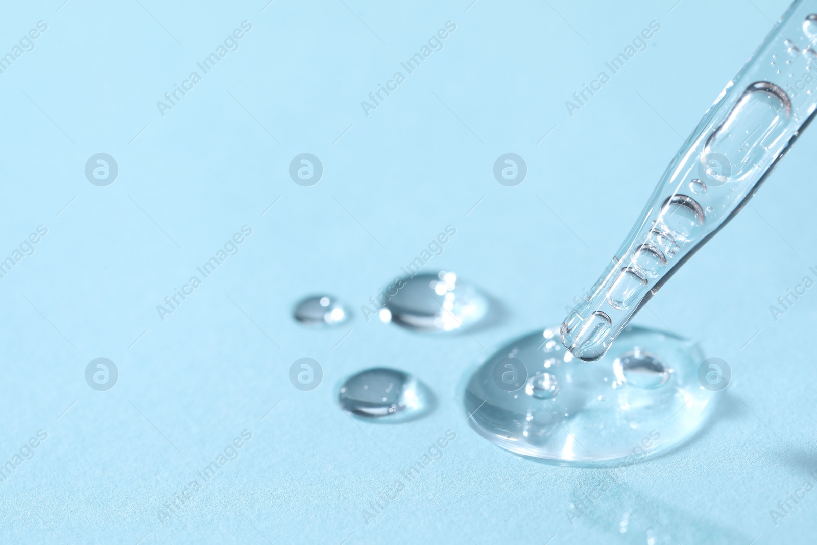 Photo of Glass pipette and transparent liquid on light blue background, closeup. Space for text