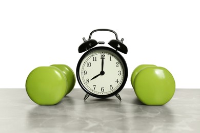 Photo of Alarm clock and dumbbells on marble table against grey background. Morning exercise