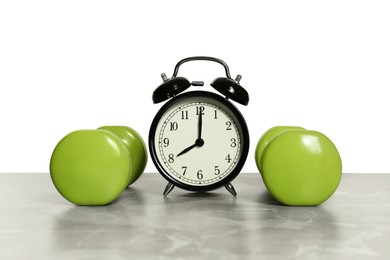 Alarm clock and dumbbells on marble table against grey background. Morning exercise