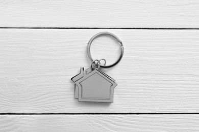 Photo of Metal keychain in shape of houses on white wooden table, top view