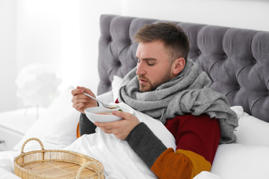 Photo of Sick young man with bowl of tasty soup in bed at home