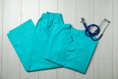 Clean scrubs and stethoscope on wooden background, top view. Medical objects