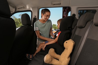 Photo of Mother fastening her son with car safety belt in child seat