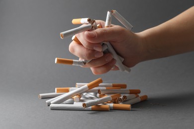 Photo of Stop smoking. Woman holding broken cigarettes over pile on grey background, closeup
