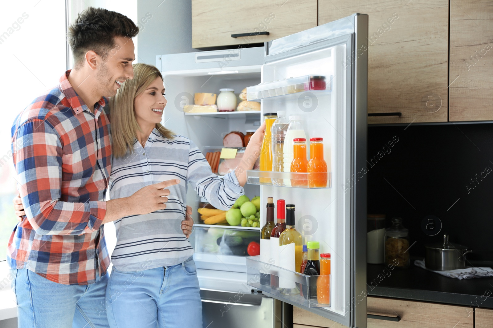 Photo of Couple taking bottle with juice out of refrigerator in kitchen