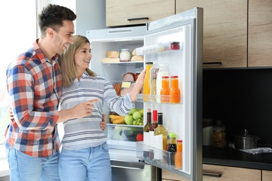 Couple taking bottle with juice out of refrigerator in kitchen