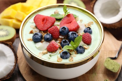 Photo of Tasty matcha smoothie bowl served with berries and oatmeal on table, closeup. Healthy breakfast