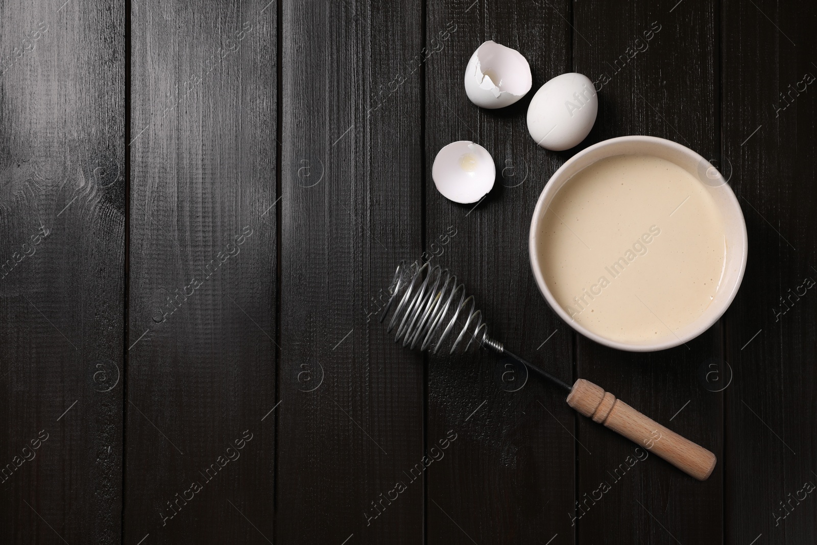 Photo of Metal whisk, dough in bowl, egg and shell on wooden table, flat lay. Space for text