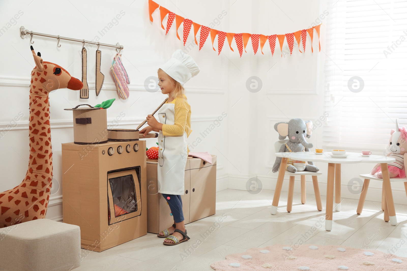 Photo of Little girl playing with toy cardboard kitchen at home