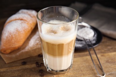 Photo of Delicious latte macchiato, croissant and scattered coffee beans on wooden table