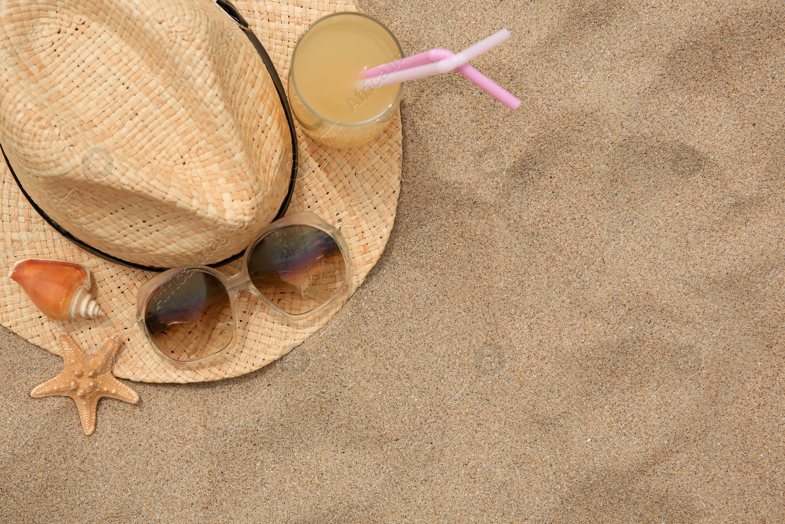Photo of Straw hat, sunglasses, refreshing drink, seashell and starfish on sand, top view with space for text. Beach accessories
