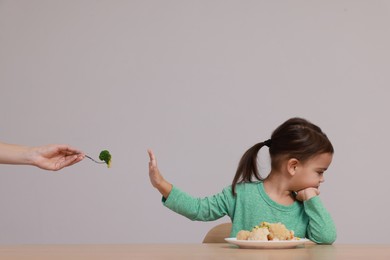 Cute little girl refusing to eat vegetables at table on grey background