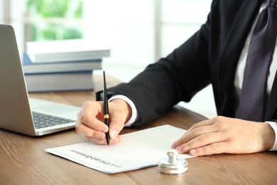 Male notary working with documents and laptop at table, closeup