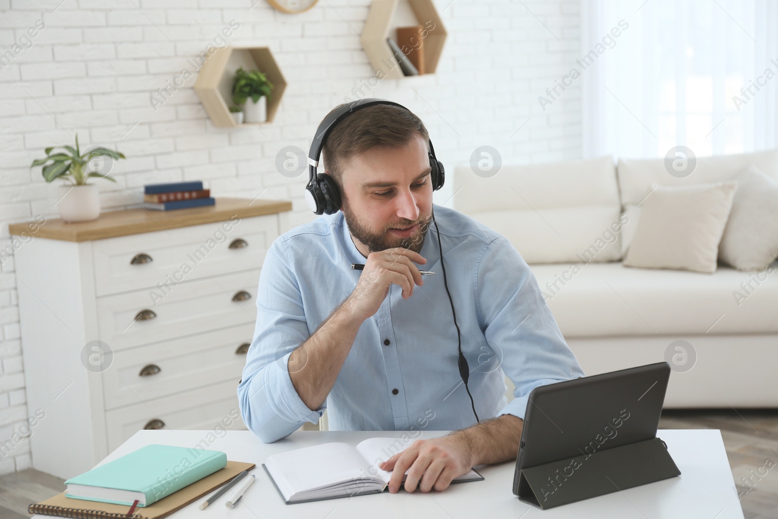 Photo of Young man watching online webinar at table indoors