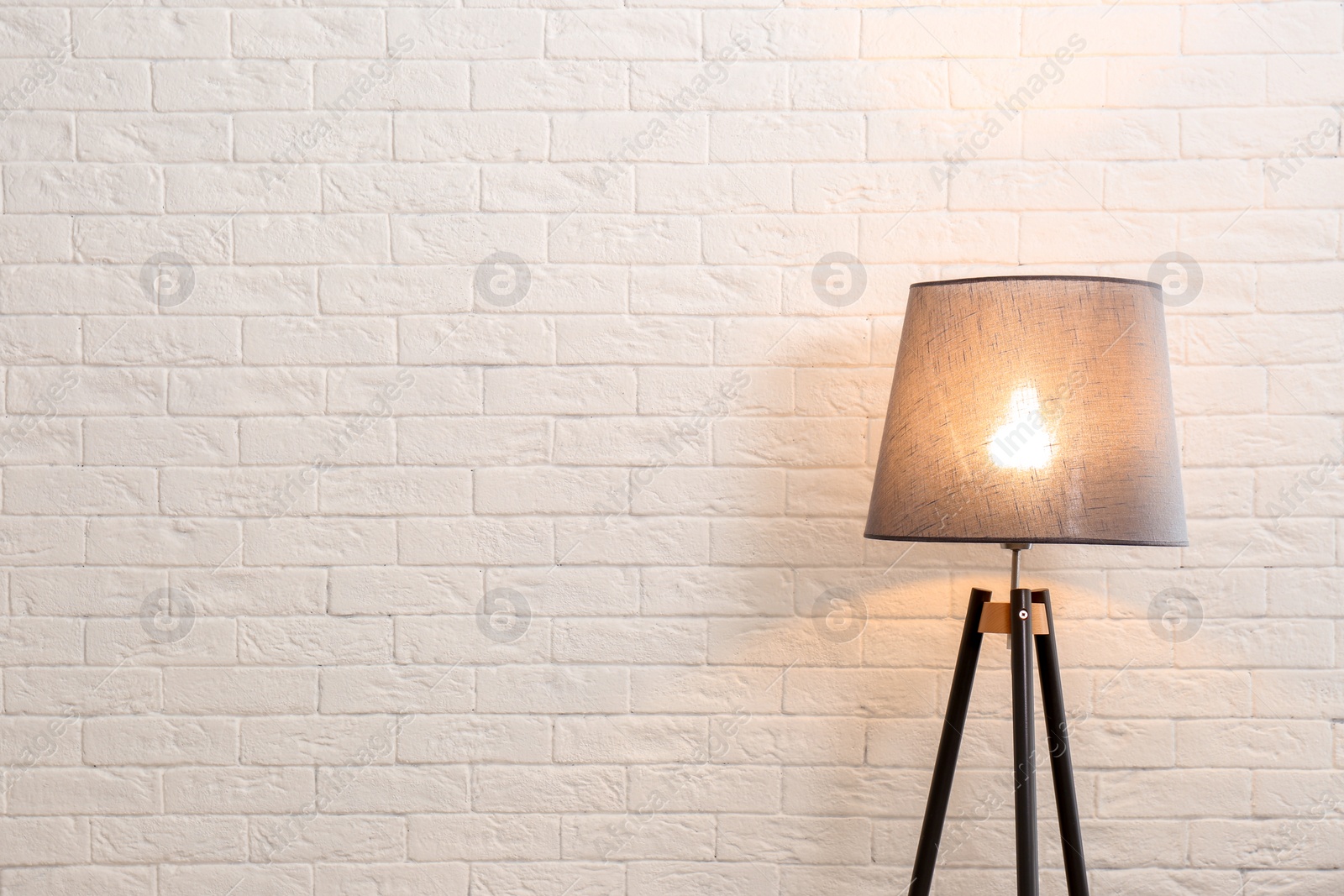 Photo of Modern floor lamp against brick wall. Space for text
