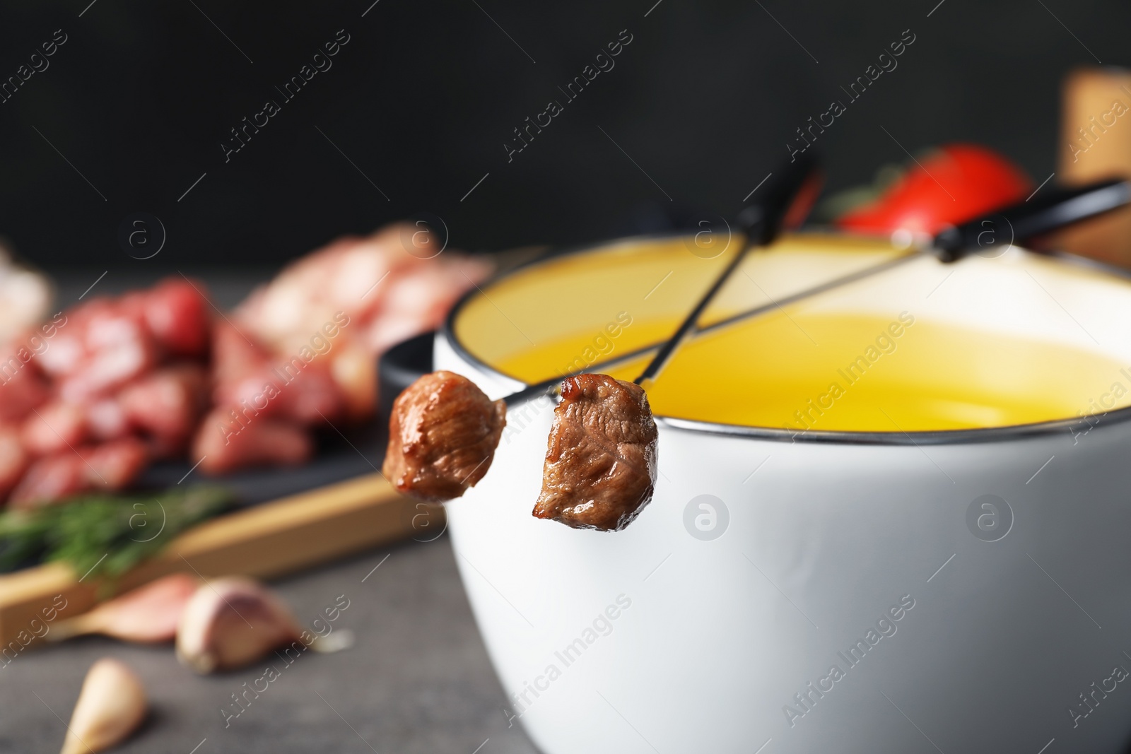 Photo of Fondue pot and forks with cooked meat on table, closeup. Space for text