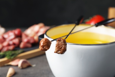 Photo of Fondue pot and forks with cooked meat on table, closeup. Space for text