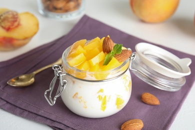 Photo of Tasty peach dessert with yogurt in glass jar on table