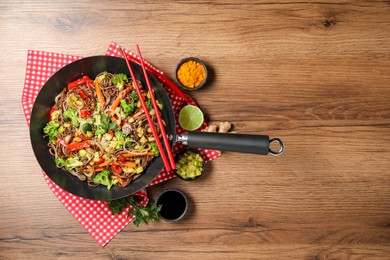 Photo of Stir-fry. Tasty noodles with meat in wok, chopsticks and ingredients on wooden table, flat lay. Space for text