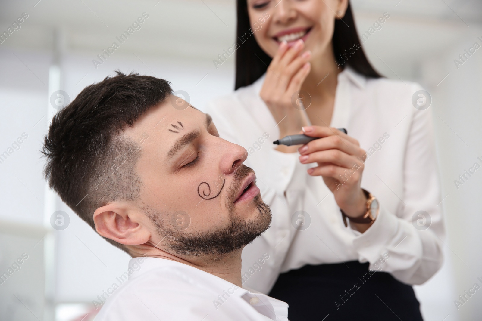 Photo of Young woman drawing on colleague's face while he sleeping in office. Funny joke