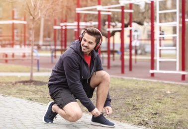 Young man with headphones tying shoelaces on sports ground