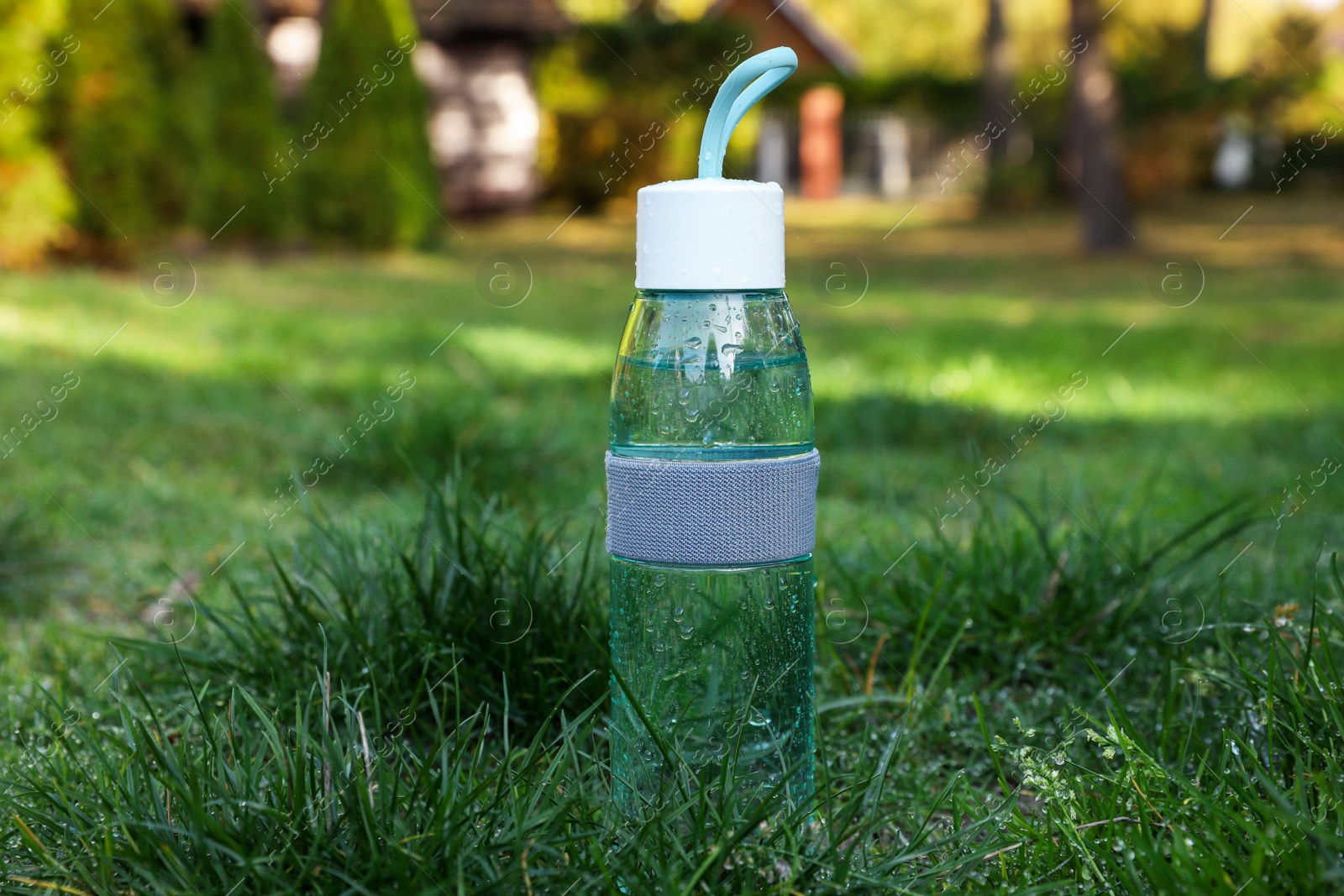 Photo of Glass bottle of fresh water on green grass outdoors