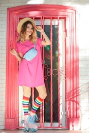 Happy girl with retro roller skates standing near pink door