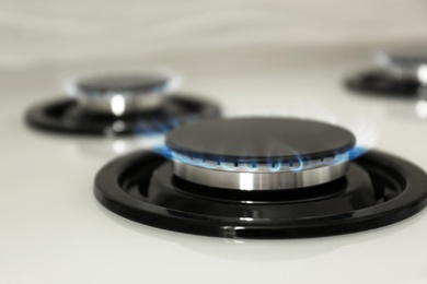 Photo of Gas burner with blue flame on modern stove, closeup