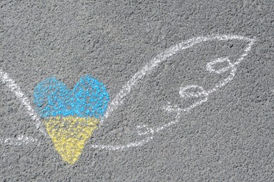 Photo of Heart and wings drawn with blue and yellow chalks on asphalt outdoors, closeup