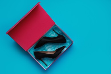 Stylish women's shoes in cardboard box on light blue background, top view. Space for text